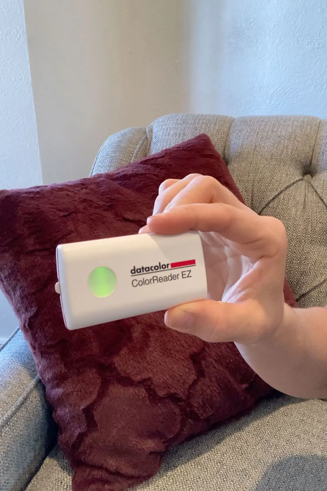 A close-up of the Datacolor ColorReader EZ device, glowing green as it scans a fabric swatch to identify the best matching color.